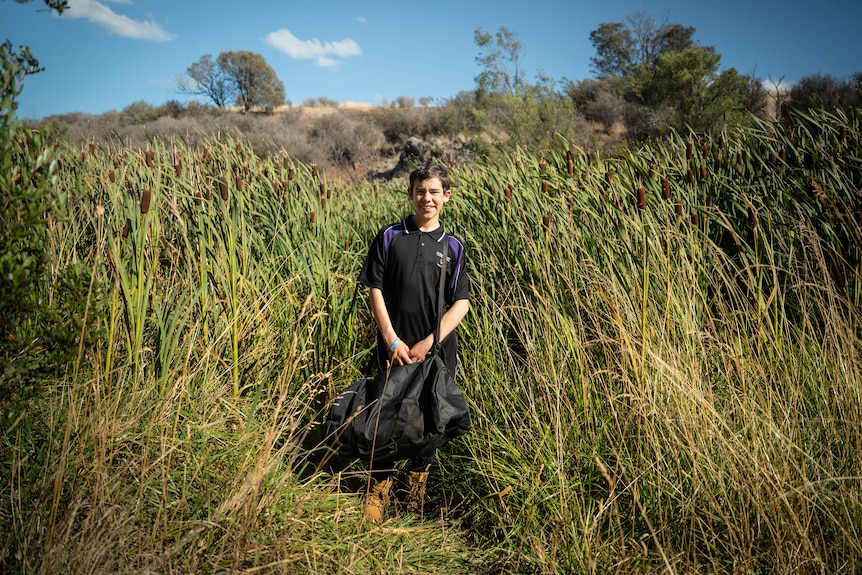 Smiling Jack in school uniform stands in front of swamp, blue sky.