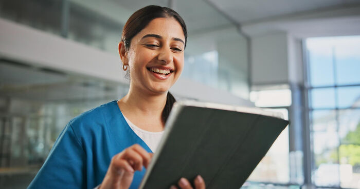 Medical professional smiling while using a tablet, illustrating cases of patients faking symptoms in healthcare settings.