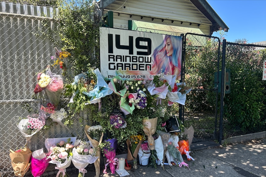 Dozens of floral bouquets and tributes by a chain metal fence.