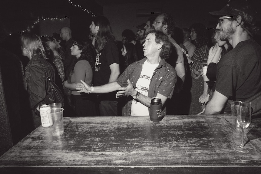 Black and white photo of man dancing next to a table amid a packed crowd