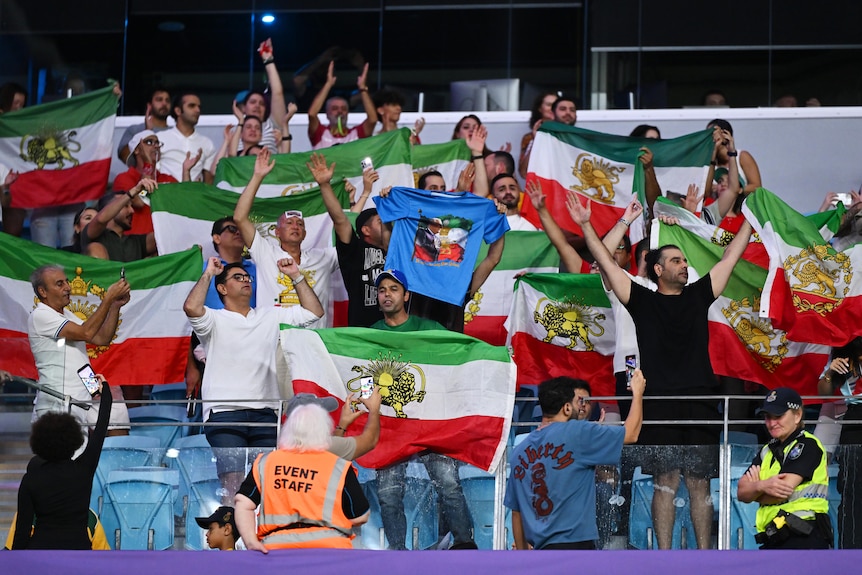 Fans hold flags which have green, white, and red horizontal stripes, with a lion and sun symbol