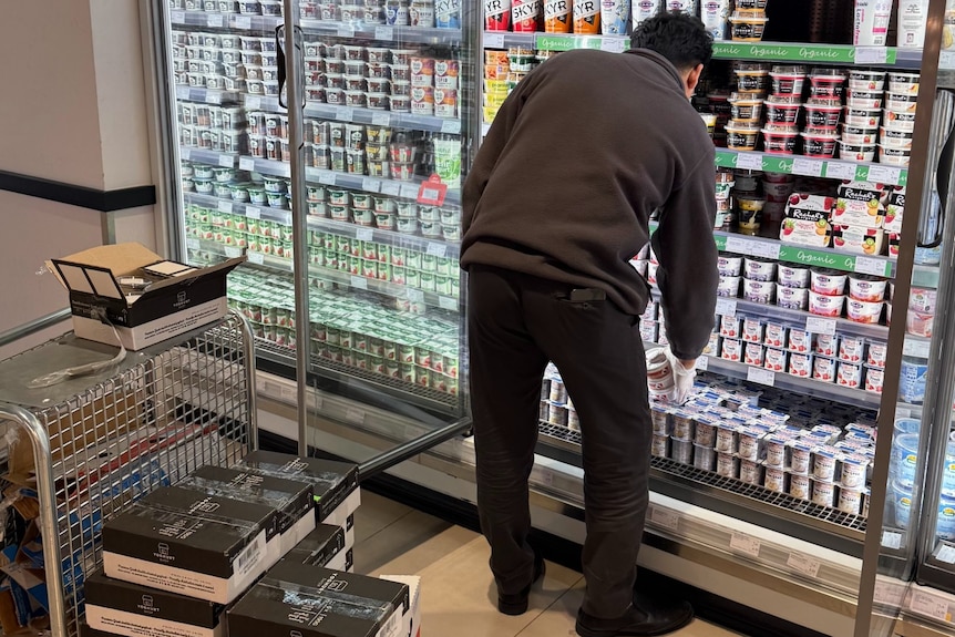 A man in dark clothing stocks shelves with yoghurt