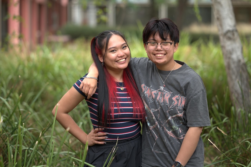 A woman with red dyed hair hugs a man in grass.