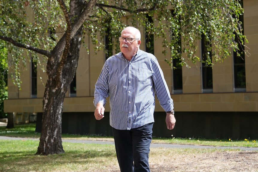 Stephen Noga wears a blue and white striped shirt and walks outside the Supreme Court in Hobart