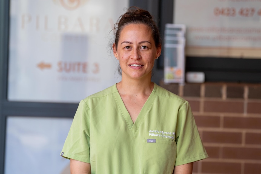 A woman in green scrubs smiles into the camera. 