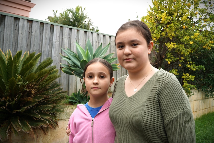 Two dark-haired girls in jumpers standing in a backyard.