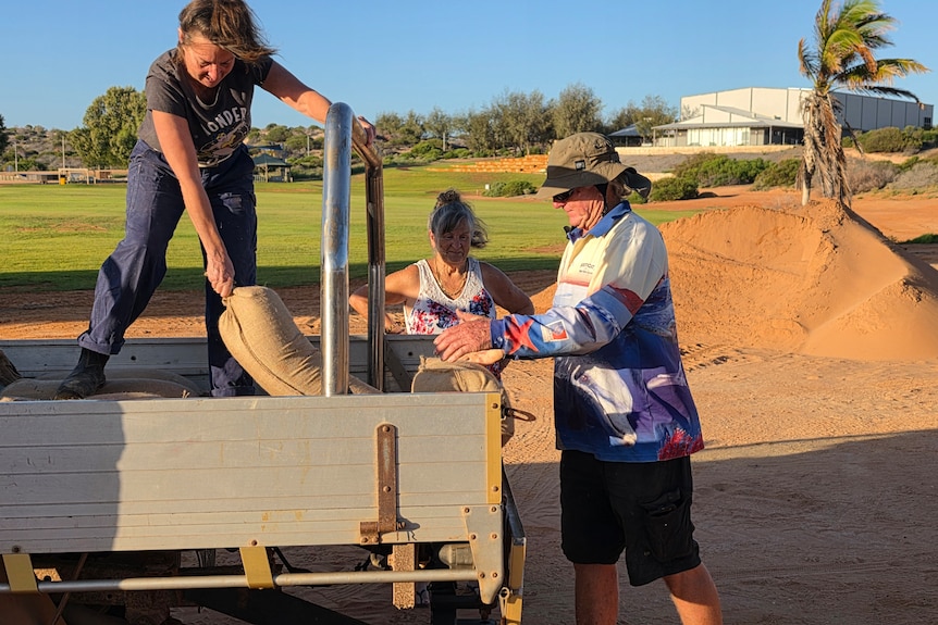 Three people unload sandbags from the back of a ute.
