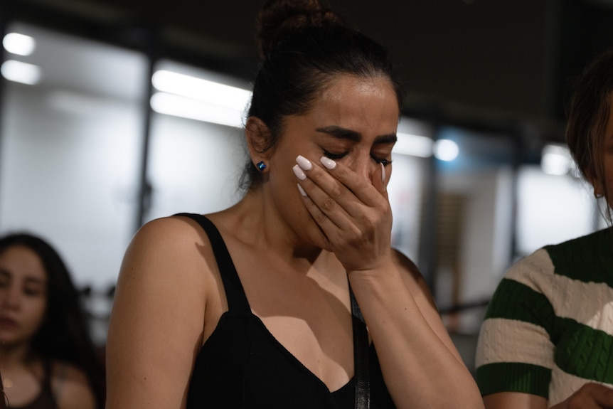 A woman has her hand over her mouth and is crying