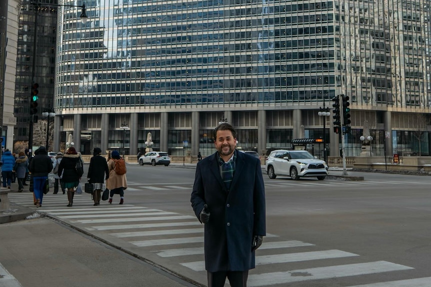 A man in a black wool coat stands on a city street