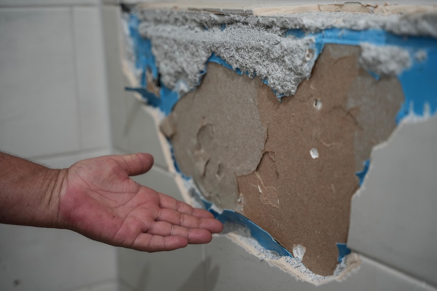A hand shows underneath tiles ripped off a wall.