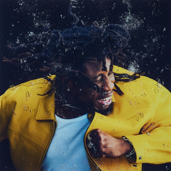 A man wearing a yellow jacket and white shirt is depicted surrounded by dynamic shattered glass effects.