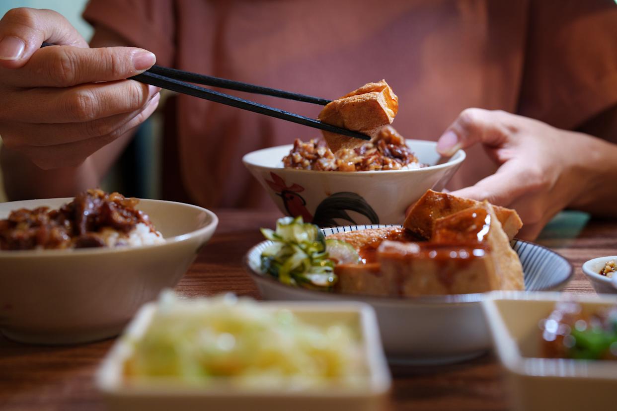 Close up shot of a young girl is seen enjoying a Taiwanese-style braised pork rice, soup, and side dishes.