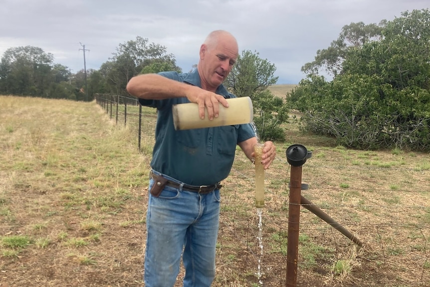 A man pours water into a plastic cylinder. 