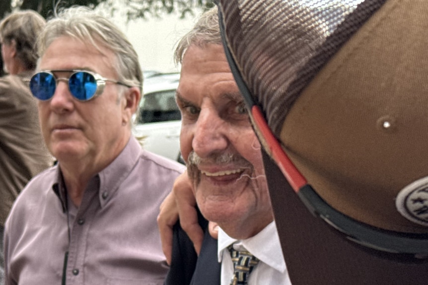 an old man walking with other people attemping to cover him from view