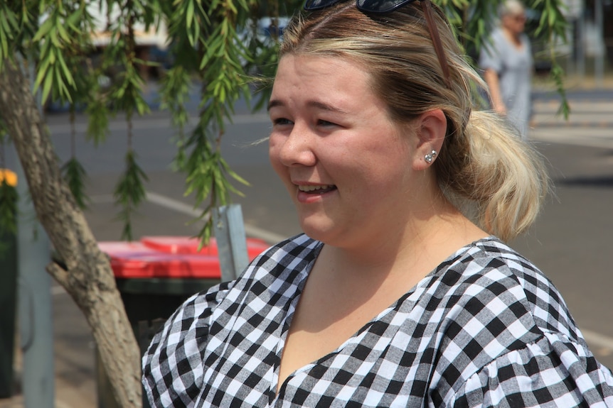 A young woman in a black-and-white checked blouse has a conversation on a footpath. 
