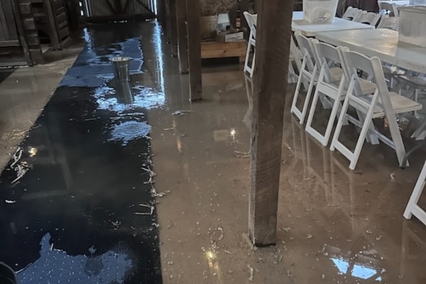 Flooded rustic event venue, water on ground and white chairs and tables.