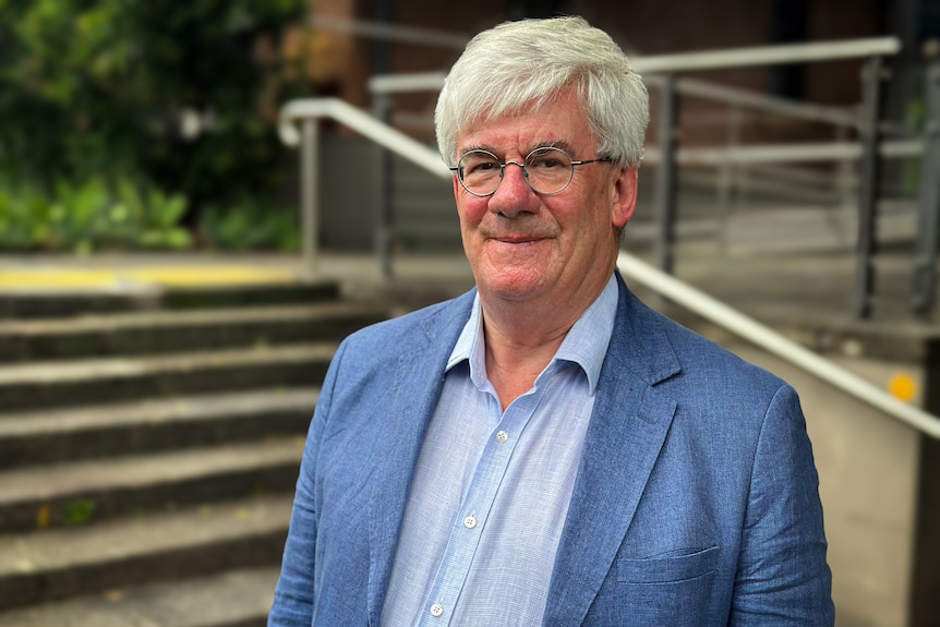 A man in a light blue shirt and jacket standing by steps outside Sydney apartments 
