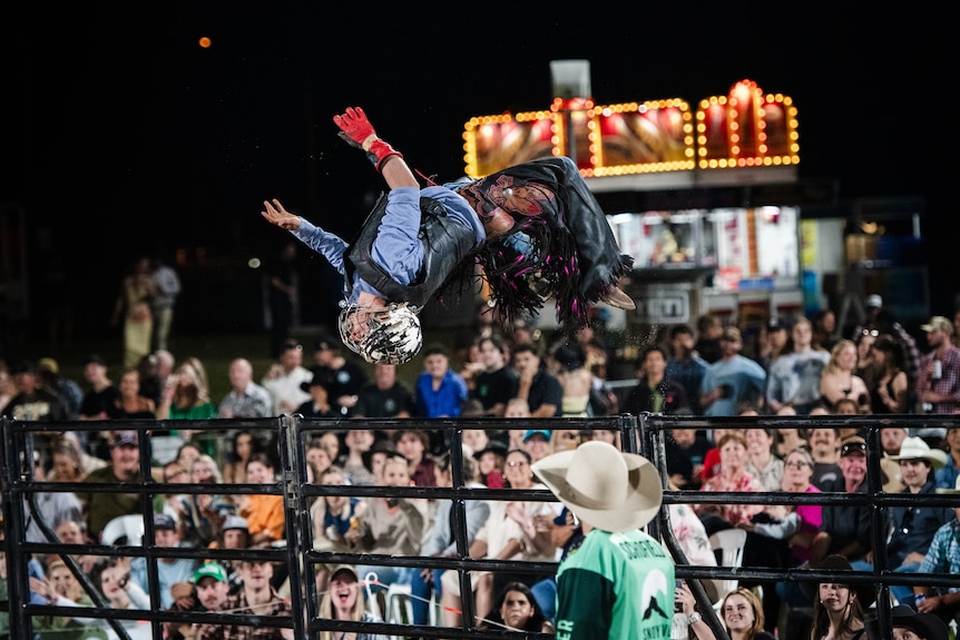 A cowboy backflips near a crowd.