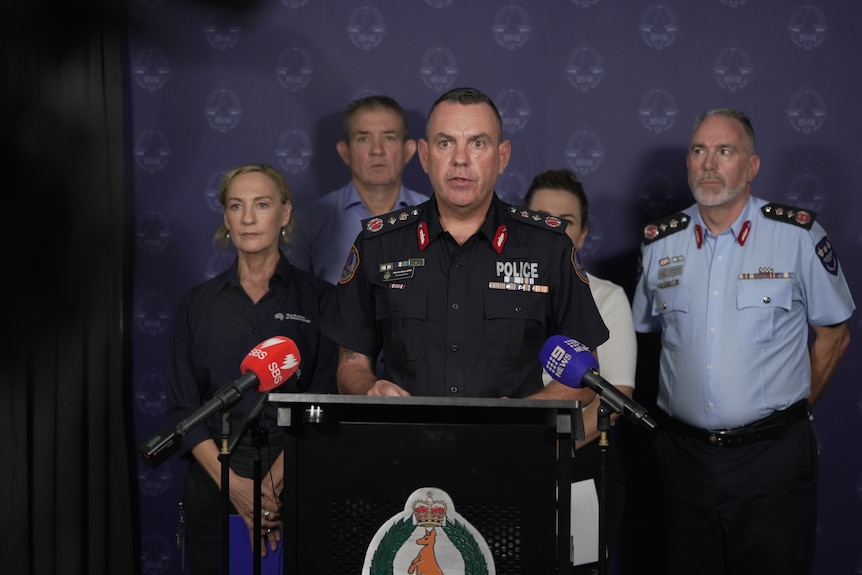 Policeman talks at press conference with four people standing behind