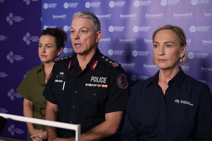 Three officials speaking into news microphones at a press conference.