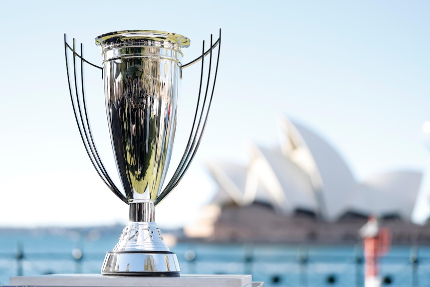 A large silver trophy is in the foreground, with the Sydney Opera House in the background.