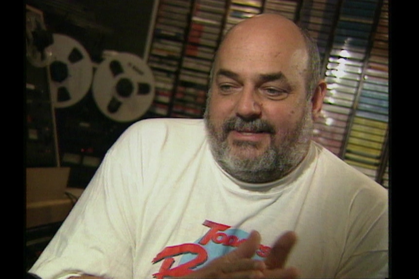 a man in a white t shirt speaking to camera