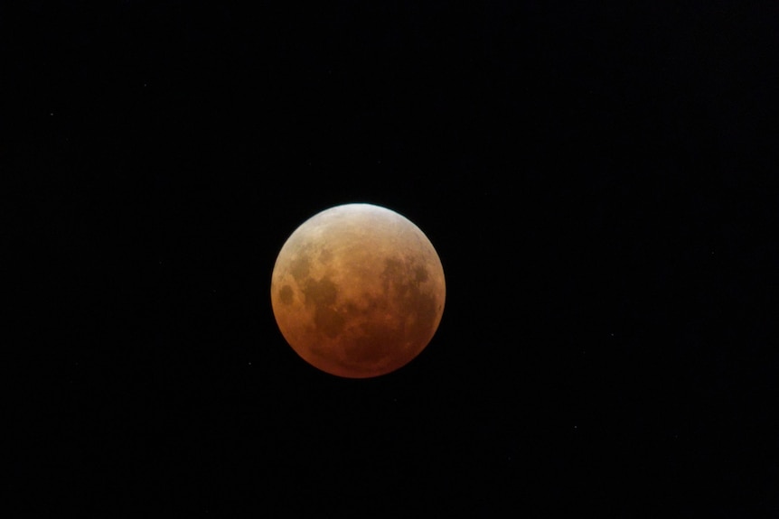 A reddish moon in a night sky