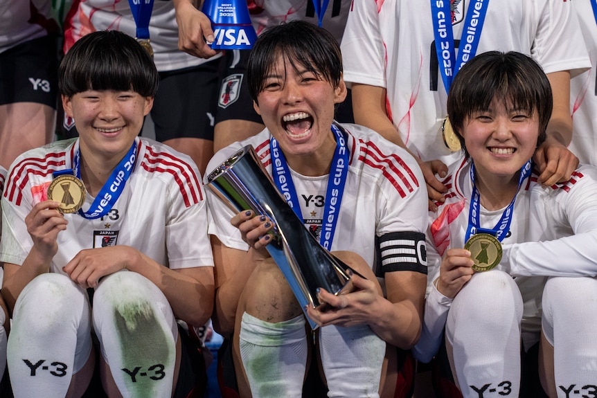 A close up image of Japan's women players, one player holds the SheBelieves trophy and smiles.