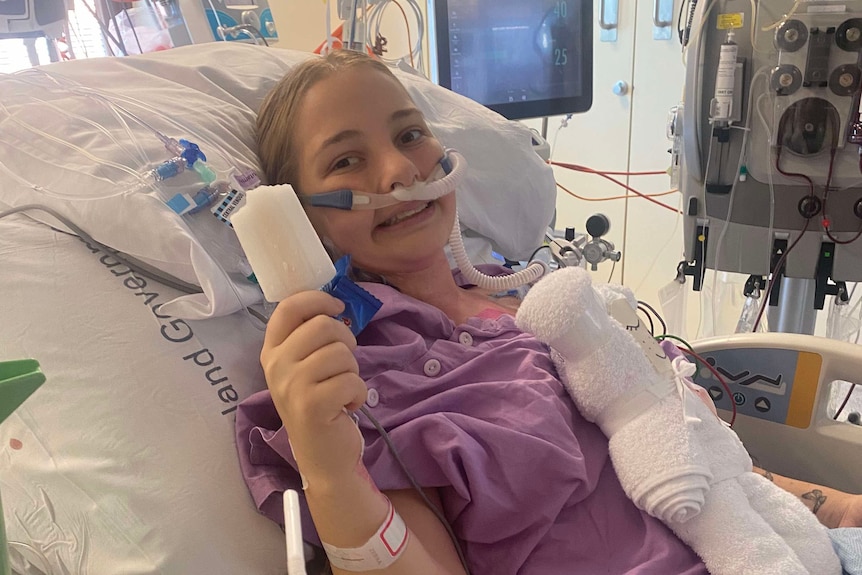 A girl in a hospital bed holding up an icy pole