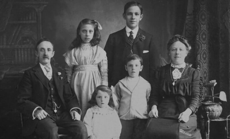 A black-and-white vintage portrait of a family with three children, a man, and a woman, all dressed in formal early 20th-century clothing, seated and standing together in a studio setting.