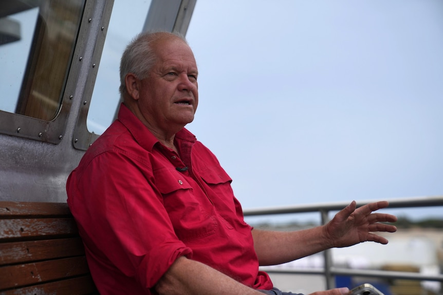 He sits on wooden bench on his ship in a red shirt