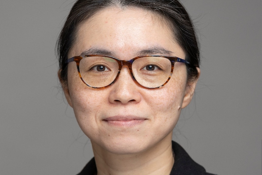 Close up image of woman with dark hair and glasses looking at camera