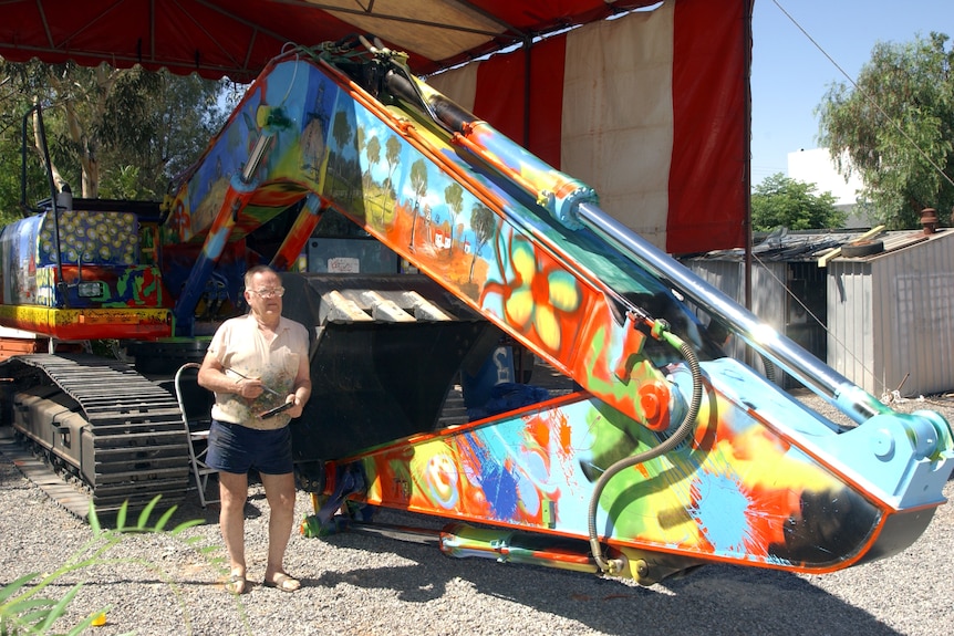 A man standing next to a construction vehicle which he painted with colourful imagery. 