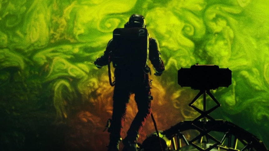 A man floats in front of a green planet in a space suit