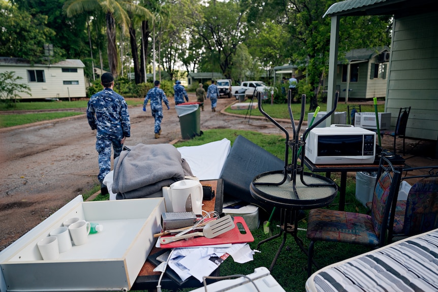 People in camoflauge uniforms walk past household furniture beside a road.