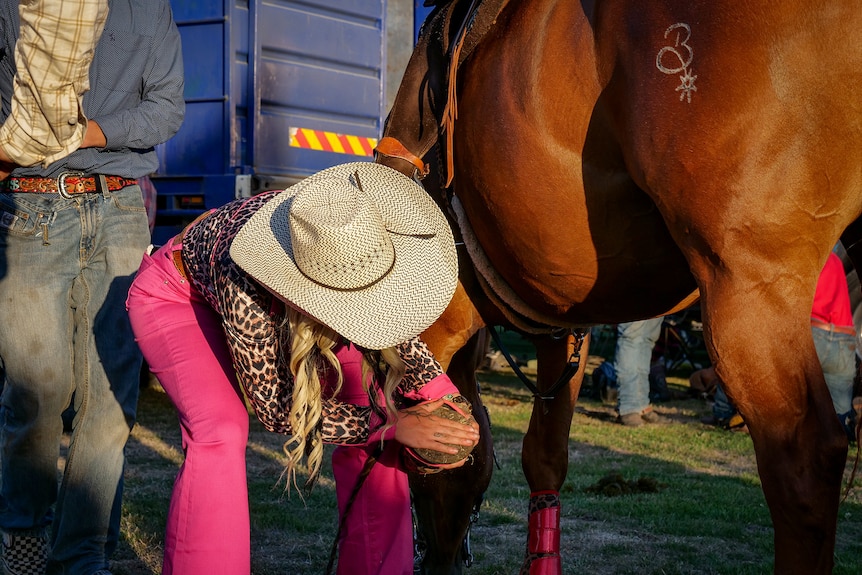 A woman looks at a horse's feet
