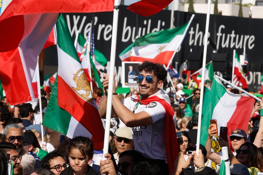 A crowd of people holding Iranian flags and a large sign that says 'We're building the future'.