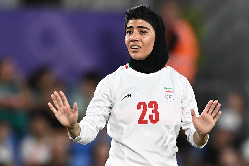 A member of the Iranian women's football team has both hands out during a game, looking to urge calm 