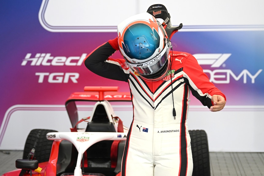 A racing driver reaches to the back of their helmet.
