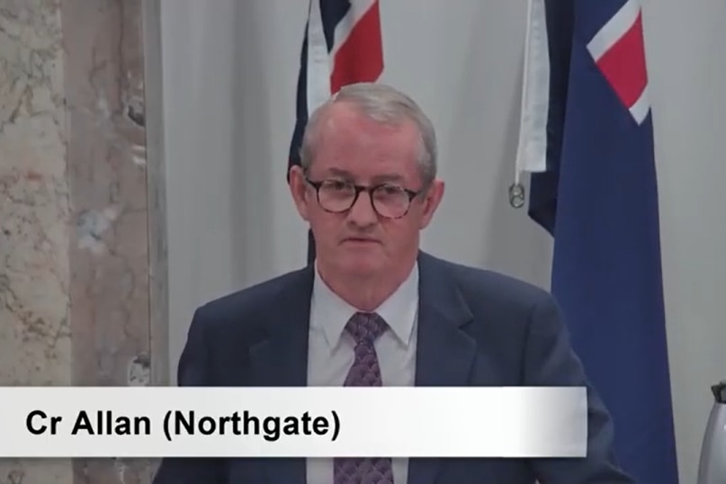 A screenshot of a man in a suit during a meeting.