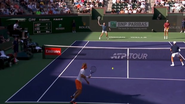 Arthur Rinderknech waves his racquet at the far end of the court as Stefanos Tsitsipas goes to hit the ball.