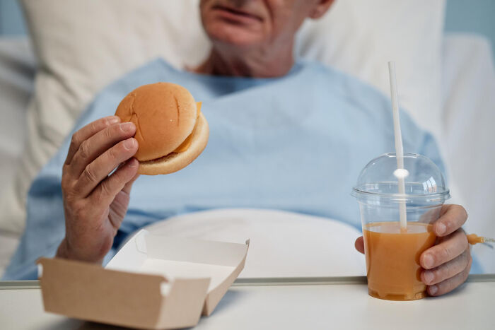Elderly patient in hospital gown holding a sandwich and juice, illustrating cases of patients faking it in medical settings.
