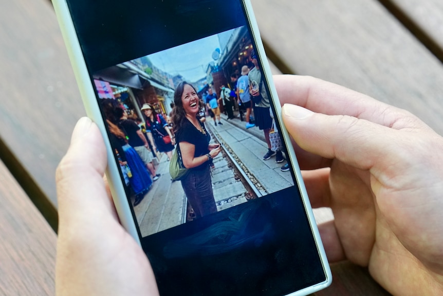 Hands holding a phone displaying a picture of a laughing woman.