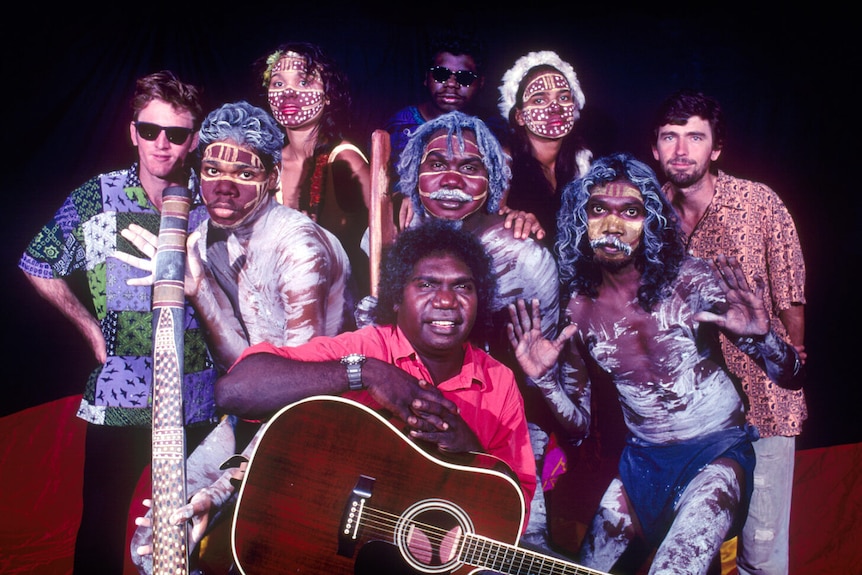 A group of Aboriginal and non-indigenous artists posing with guitars and didgeridoos.