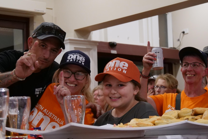 a group of people with one nation hats on smile with their fingers signaling number one