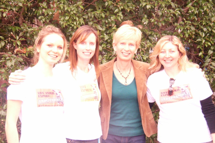 Four women stand together, smiling.