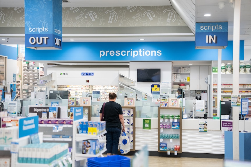 A script counter at a pharmacy, with an unidentifiable man waiting in line.