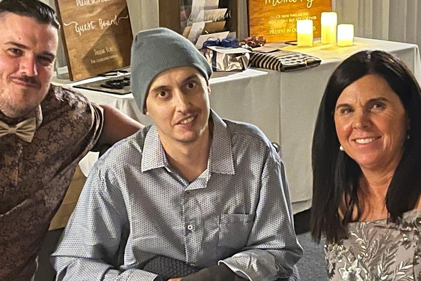A man with a bow tie, a man wearing a beanie hat and a woman seated together. 