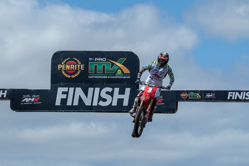 A female motocross rider soaring through the air over the finish line jump.