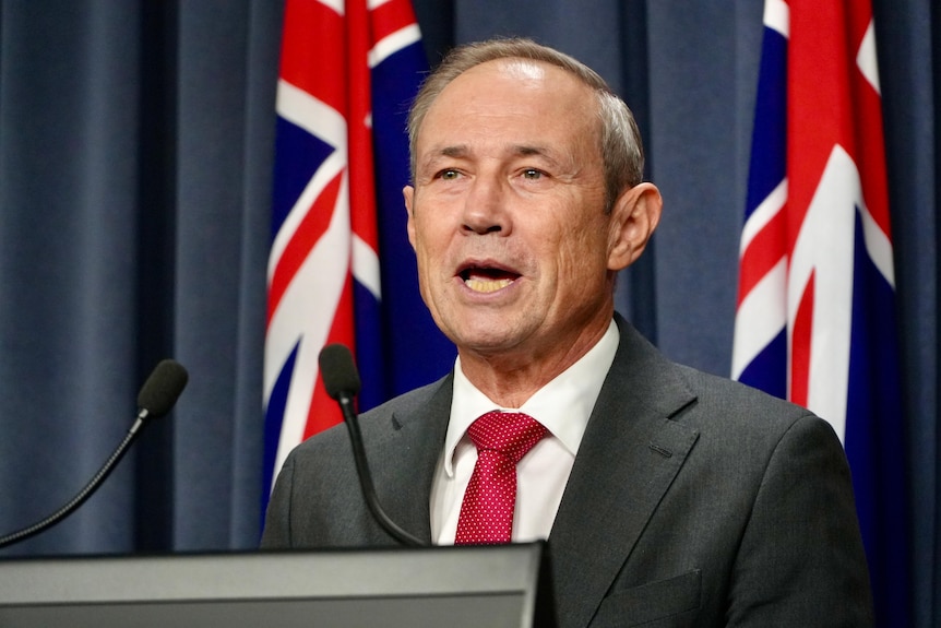 Roger Cook stands at a podium with the Australian and WA in the background.